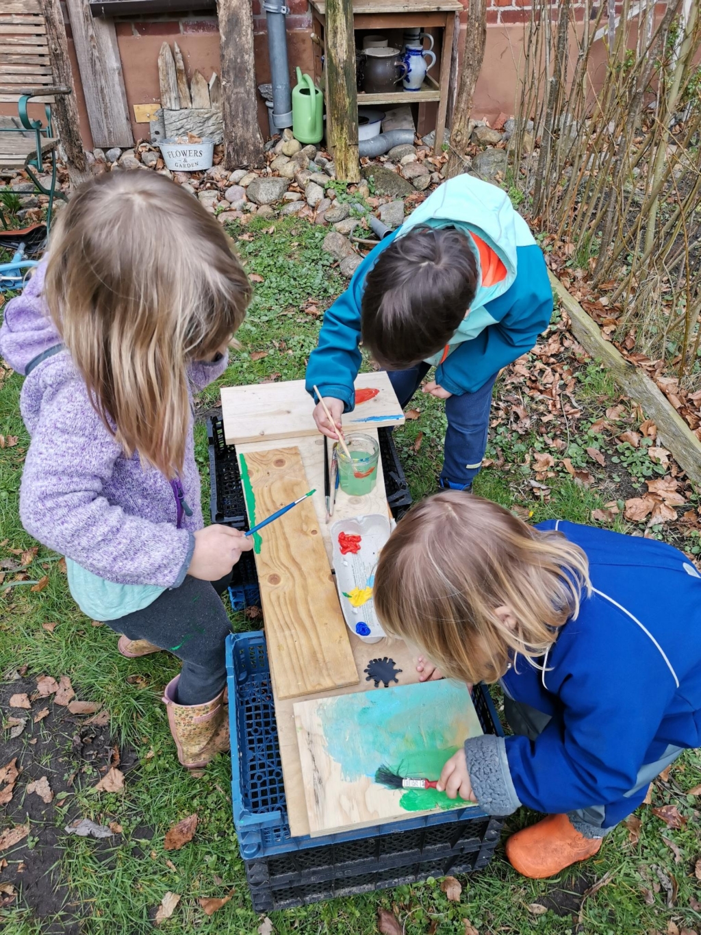 Drei Kinder malen mit Pinsel auf Holz draußen