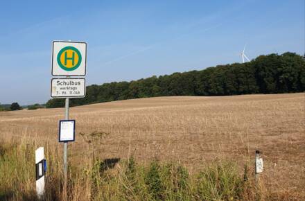 Bushaltestellenschild vor Feldlandschaft