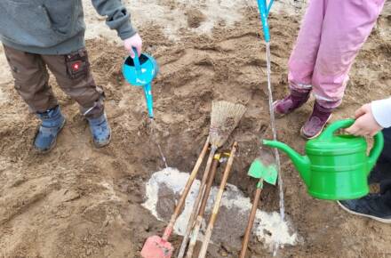 Kinder gießen Wasser im Sand mit Werkzeugen.